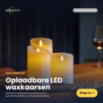 De LED wax kaarsen set 3 kaarsen DORSETTO gloeit warm op een houten tafel en brengt een gezellige sfeer. Een wijnglas en glasbak verschijnen zacht vervaagd op de achtergrond.