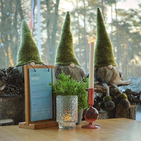 Drie pluchen kabouters met groene hoeden zitten achter een lunchmenu en een glazen kandelaar met daarin een 3D oplaadbaar LED-thee/waxinelichtje (175 uur, afstandsbediening, timerfunctie, 12 stuks); op de achtergrond verschijnen dennenappels en bomen.