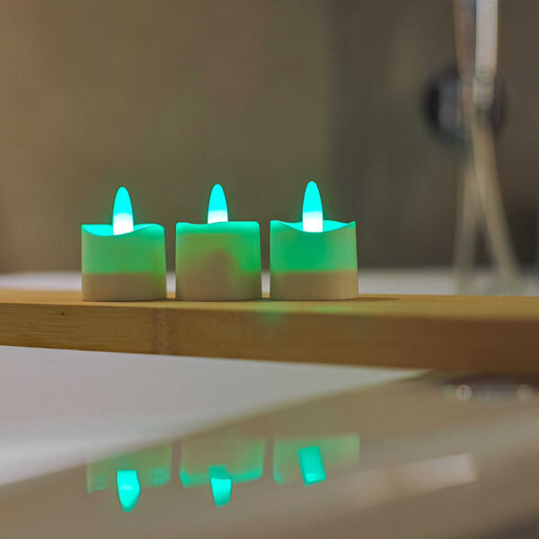 Drie RGB LED-Waxine/theelichtjes waterdicht (oplaadbaar, 68 uur, met afstandsbediening) zijn geplaatst op een houten oppervlak boven een reflecterend wit vlak, in zachte verlichting.