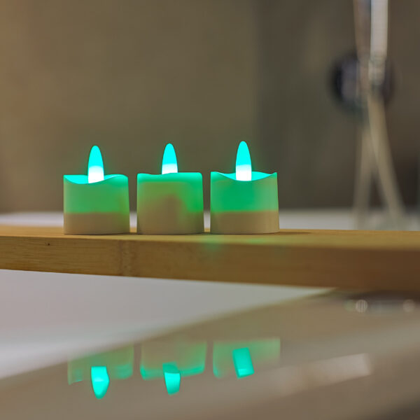 Drie kleine, witte RGB LED-Waxine/theelichtjes oplaadbaar waterdicht staan op een rij op een houten dienblad, elk met groen oplichtende vlammen die weerspiegeld worden op het gladde witte oppervlak eronder.