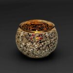 De Theelichthouder zwart 9 CM DORSETTO gloeit warm als er een kaars in brandt. Het ronde mozaïekglas bestaat uit gouden, zilveren en spiegelende fragmenten tegen een effen donkere achtergrond.