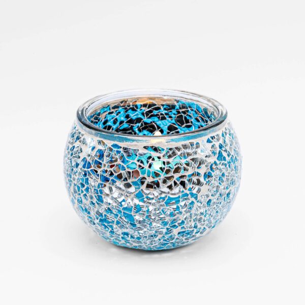 KORTING75 11 De Theelichthouder 9 CM Dorsetto lichtblauw is een ronde glazen theelichthouder met een mozaïek van lichtblauwe en zilveren scherven, waardoor een reflecterend en kleurrijk oppervlak ontstaat tegen een witte achtergrond.