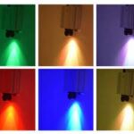 Zes panelen tonen de LED Sterrenhemel RGB hoge kwaliteit (180 sterren) met afstandsbediening, die elk levendige groene, gele, paarse, rode, blauwe of cyaan spots projecteren tegen een witte muur in twee nette rijen van drie.