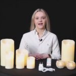 Een vrouw in een wit shirt zit aan een zwarte tafel met de DORSETTO LED waxinelichtjesset 2 maten warm wit oplaadbaar, twee glitterende waxinelichthouders, een afstandsbediening en een oplaadkabel, tegen een zwarte achtergrond met het Dorsetto-logo.