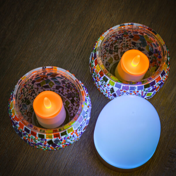 Twee kandelaars van mozaïekglas met gloeiende LED-kaarsen staan op een houten oppervlak naast de Tafellamp DORSETTO oplaadbaar 105 uur, een waterdichte, ovale wit-gouden lamp met afstandsbediening.