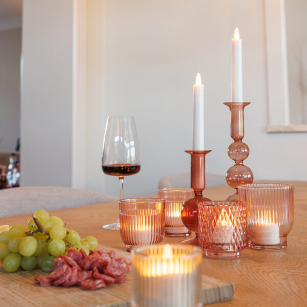 Een houten gedekte tafel met Dinerkaars 197mm LED DORSETTO oplaadbaar 130 uur warm wit (12 stuks, met afstandsbediening), een glas rode wijn, groene druiven en vleeswaren creëert een warme, gezellige sfeer.