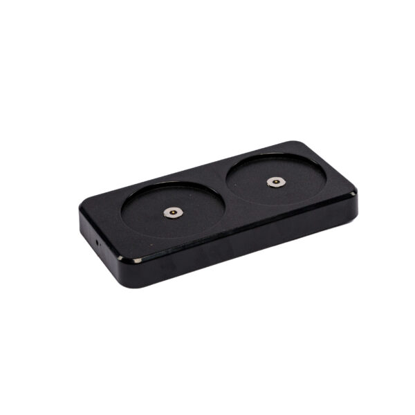 Het Oplaadstation DORSETTO is een zwart rechthoekig oplaadstation met twee ronde sleuven en metalen contacten, ontworpen voor het opladen van twee oplaadbare LED tafellampen. De achtergrond is effen wit.