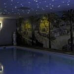 Een binnenzwembad is voorzien van een muurschildering met een dorpsscène en een LED Sterrenhemel RGB hoge kwaliteit (180 sterren) met afstandsbediening, waardoor een nachtelijk sterrenhemel ontstaat. Een wit standbeeld staat sierlijk aan de rand van het zwembad.