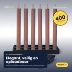 Zes hoge, roze LED dinerkaarsen (250 mm) staan in een rij op een zwarte standaard. Set van 6, oplaadbaar, dimbaar en bedienbaar met afstandsbediening. Promotie: tot 400 uur brandtijd. Lichtgrijze achtergrond met gele 'Shop nu' knop.