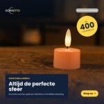 Een set van 12 zachtroze oplaadbare waxinelichtjes met afstandsbediening staat op hout. De onscherpe achtergrond benadrukt hun sfeer. Nederlandse tekst noteert tot 400 uur merkduur. Een "Shop nu" knop nodigt uit tot aankoop.